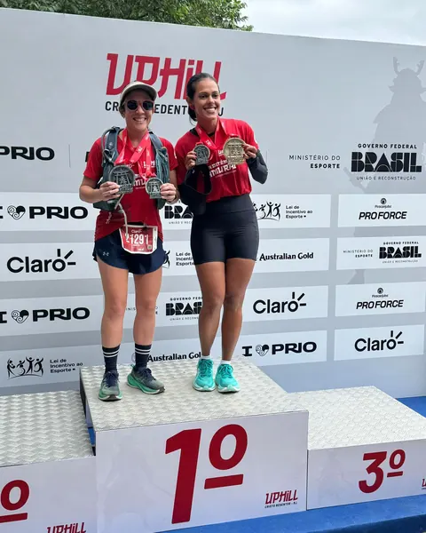 Duas atletas de uniforme vermelho no pódio, em primeiro lugar, com medalhas.