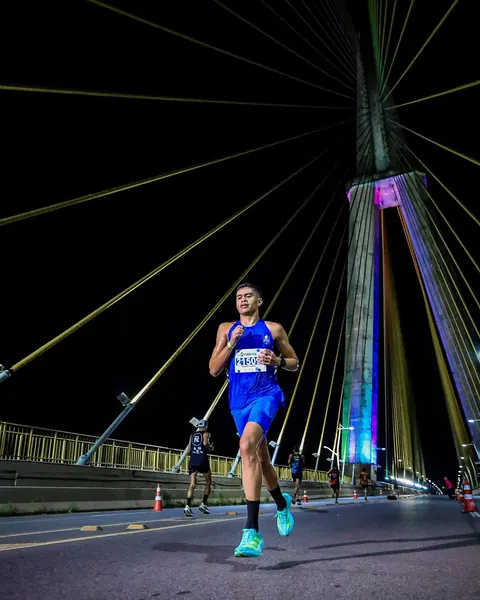 Atleta correndo à noite em ponte iluminada.