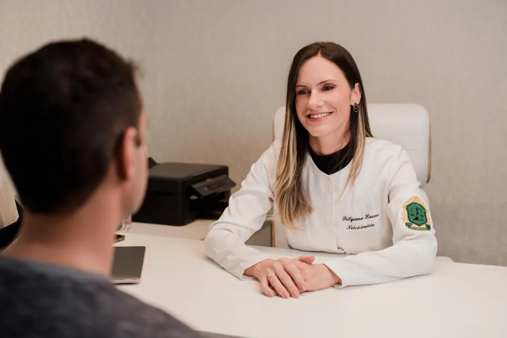 Pollyanna Hauser de jaleco, em consulta com um paciente no consultório.
