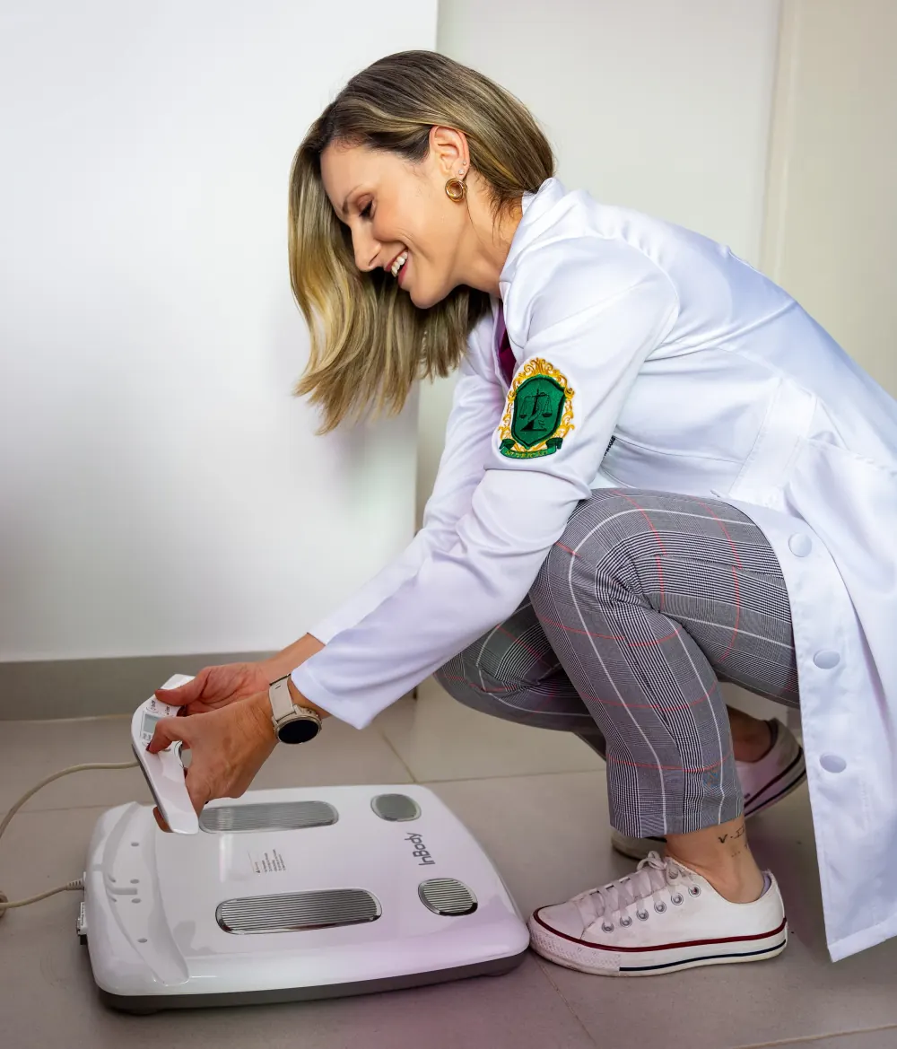 Pollyanna Hauser, de jaleco, preparando a balança de bioimpedância InBody no consultório.